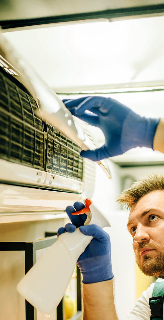 Repairman in uniform cleans the air conditioner